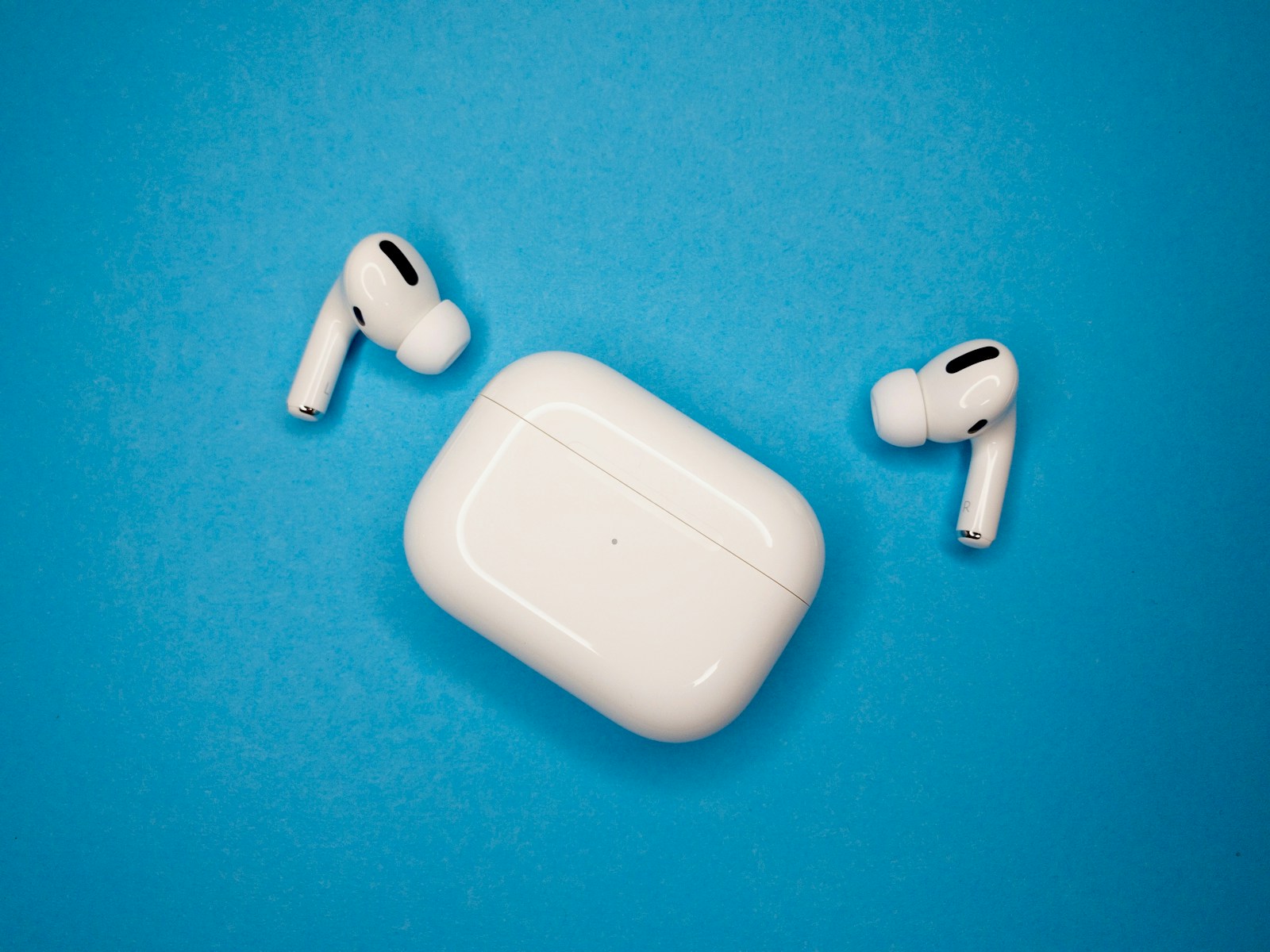 青い背景に置かれた白いAirPods Proと充電ケース