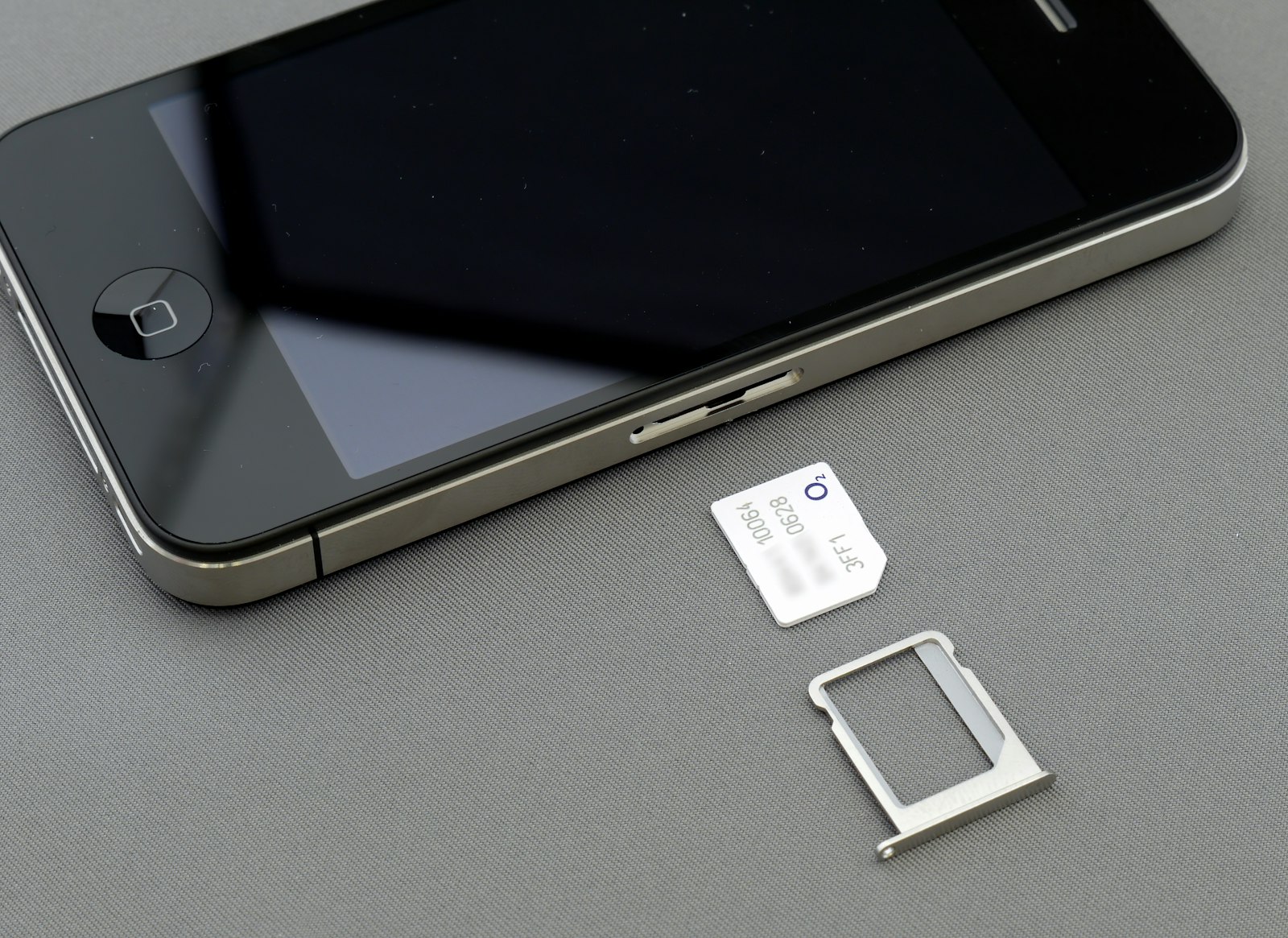An iPhone lying beside its removed SIM tray and a SIM ejector tool