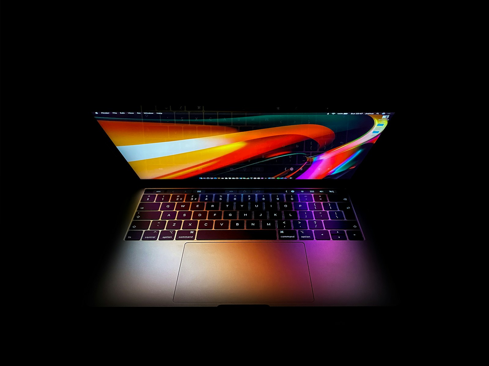 An open MacBook Pro in a dark room, its screen showing a colourful abstract wallpaper