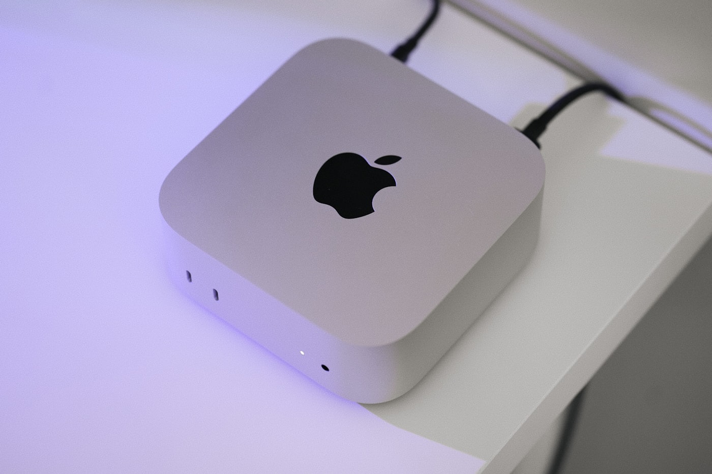 A current-generation Mac mini on a white desk, photographed from above; the M4 and M6 models look the same externally.