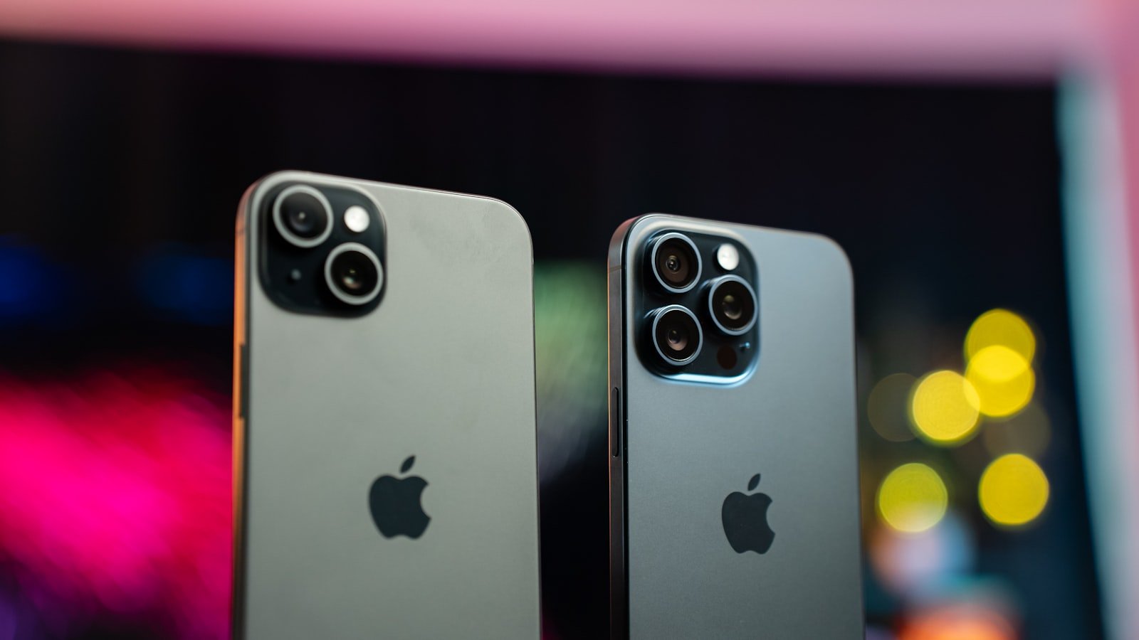 Two iPhones standing side by side, seen from the back, in front of a blurred colourful background.